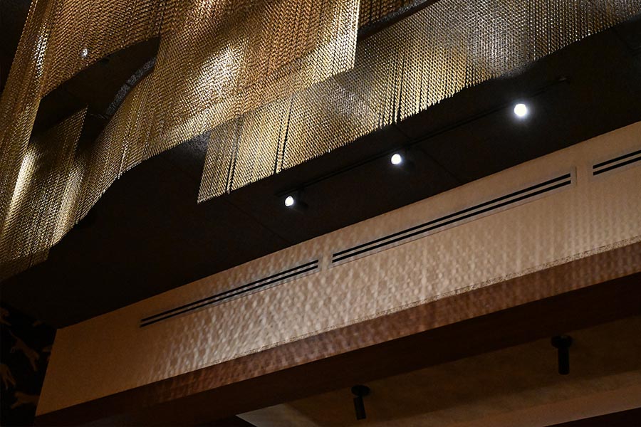 ceiling-decorated-with-long-draped-sheets-of-golden-metallic-mesh-hanging-above-a-dark-wall-serafina-restaurant
