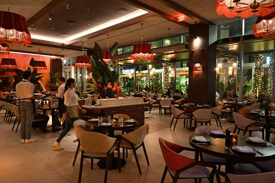 restaurant-features-white-clothed-staff-moving-between-round-wooden-tables-surrounded-by-lush-indoor-greenery-and-large-red-fringed-chandeliers-serafina-miami