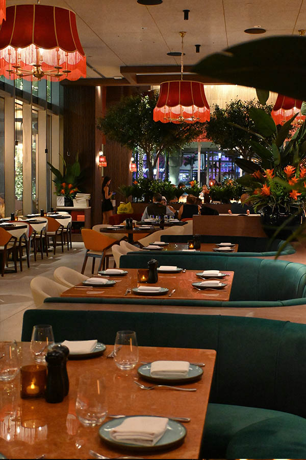 spacious-restaurant-dining-room-features-long-teal-velvet-booths,-marble-topped-tables-set-with-plates-and-candles-serafine-miami