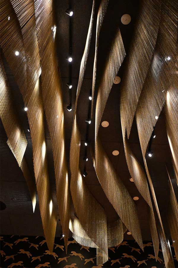 striking-ceiling-installation-features-long-flowing-swathes-of-golden-metallic-mesh-draped-in-undulating-waves-beneath-recessed-spotlights