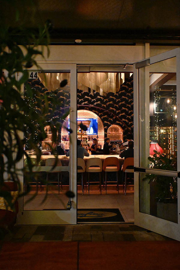 view-through-glass-doors-reveals-a-stylish-bar-area-with-leopard-print-wallpaper-and-an-arched-back-bar-serafina-miami