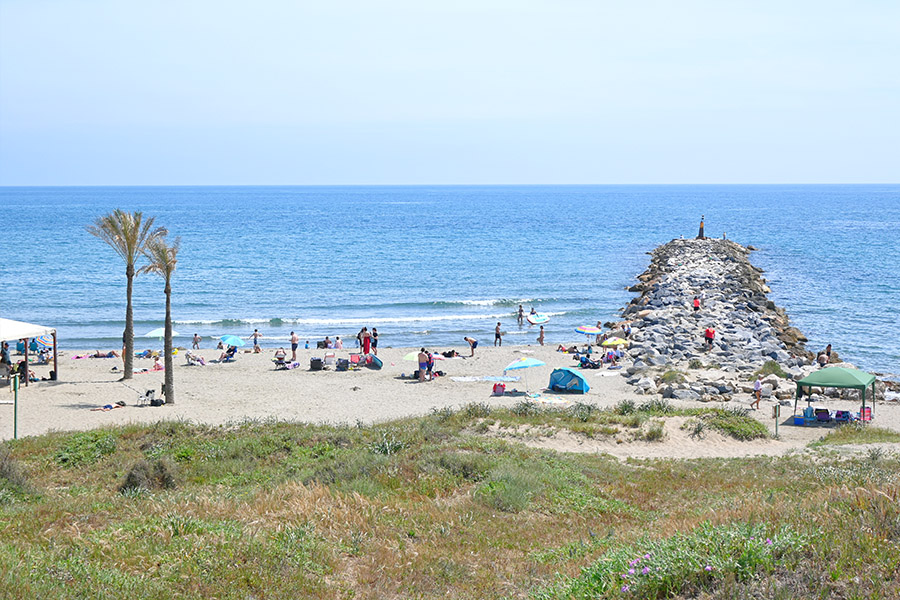 People-relaxing-on-the-sand-near-a-rock-breakwater-Spain-beaches-Playa-Cabopino