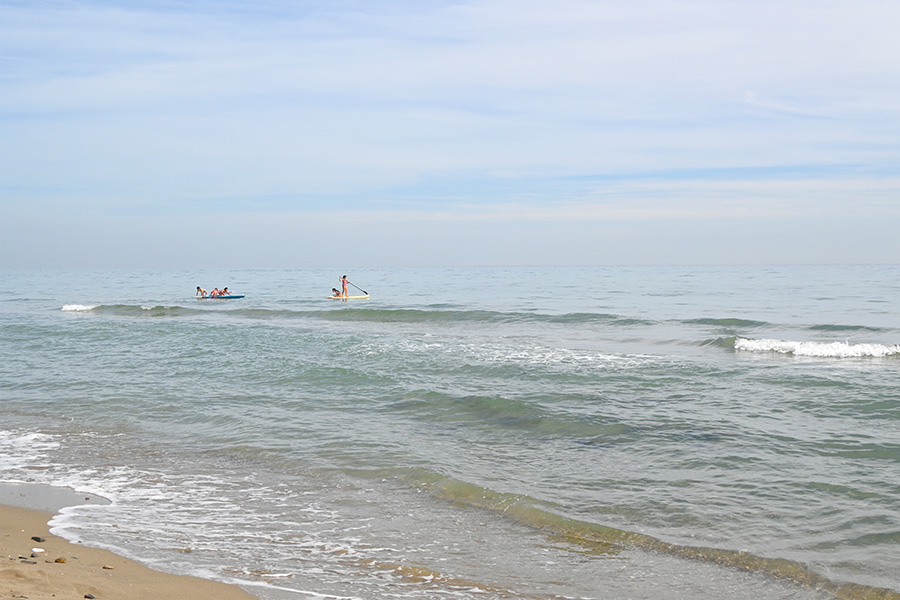 Several-people-paddling-on-surfboards-and-small-boats-in-the-calm-blue-ocean-water-playa-las-canas-marbella
