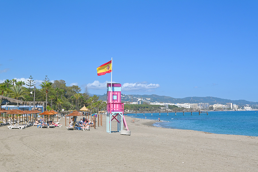 spanish-flag-flying-above-colorful-beach-tower-with-distant-mountains